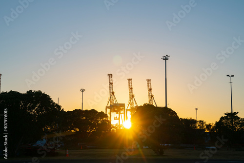 Container cranes on Port of Tauranga facility backlit by rising sun at Sulphur Point in city.