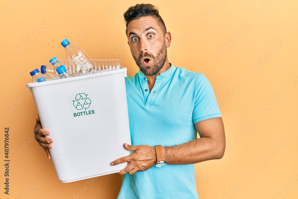 Handsome man with beard holding recycling wastebasket with plastic bottles scared and amazed with open mouth for surprise, disbelief face Handsome man with beard holding recycling wastebasket with plastic bottles scared and amazed with open mouth for surprise, disbelief face