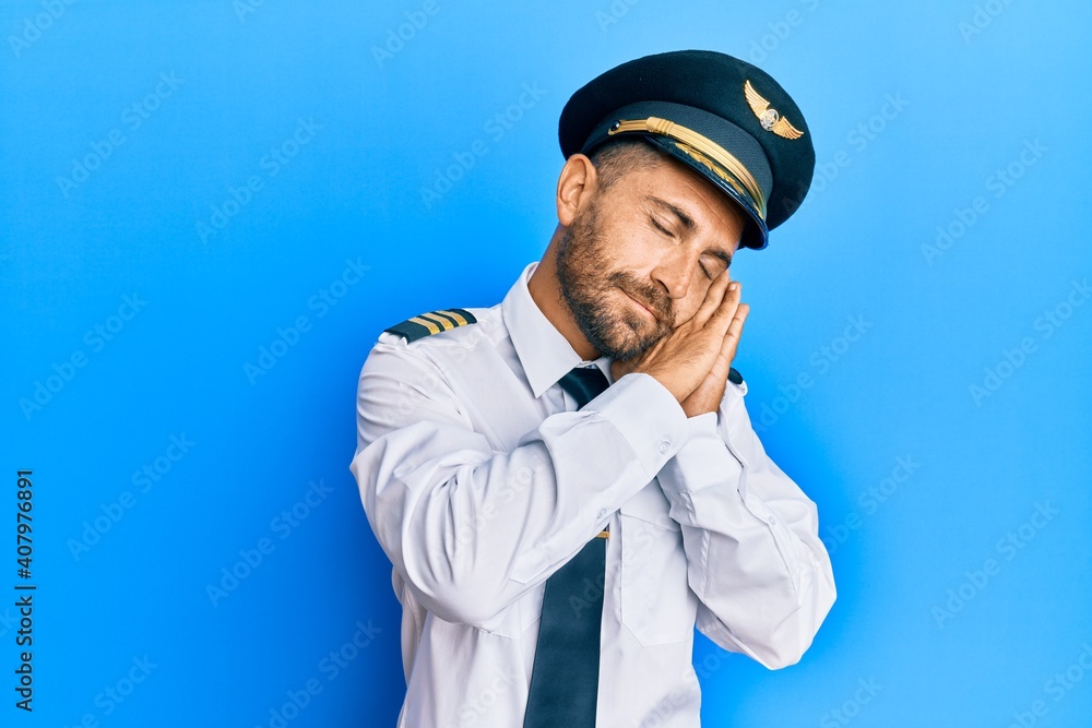 Handsome man with beard wearing airplane pilot uniform sleeping tired dreaming and posing with hands together while smiling with closed eyes. Handsome man with beard wearing airplane pilot uniform sleeping tired dreaming and posing with hands together while smiling with closed eyes.