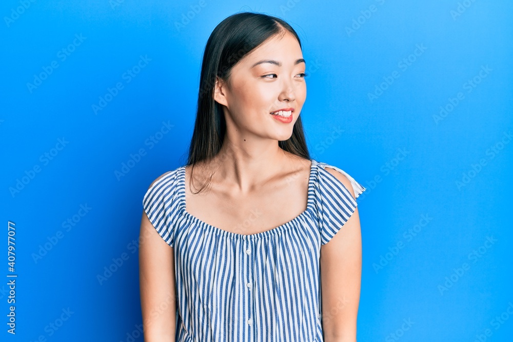 Fototapeta premium Young chinese woman wearing casual striped t-shirt looking away to side with smile on face, natural expression. laughing confident.