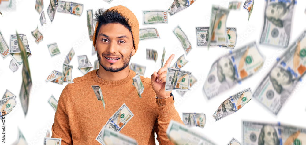 Handsome latin american young man wearing winter sweater and wool hat showing and pointing up with finger number one while smiling confident and happy. Handsome latin american young man wearing winter sweater and wool hat showing and pointing up with finger number one while smiling confident and happy.