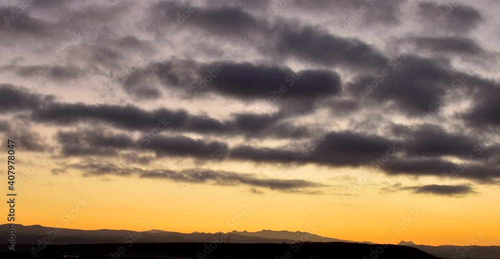 A clouded sky glows in yellow and orange at the horizon at sunrise near San Quintin, Baja California, Mexico