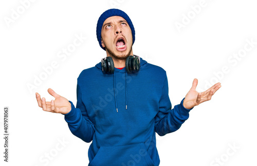 Hispanic young man wearing sweatshirt and wool hat crazy and mad shouting and yelling with aggressive expression and arms raised. frustration concept.