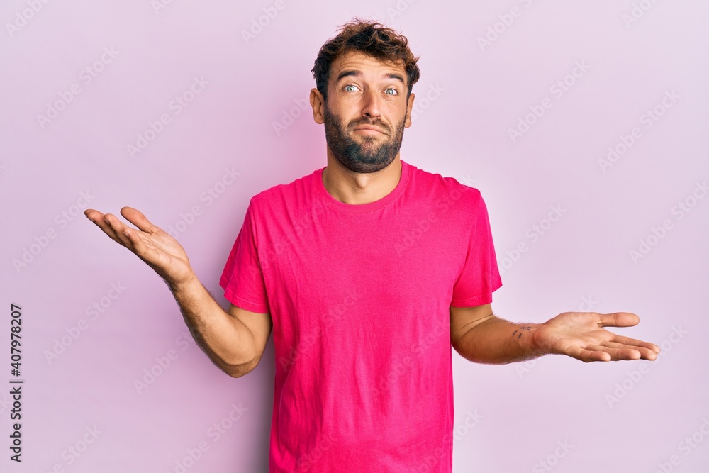 Handsome man with beard wearing casual pink tshirt over pink background clueless and confused expression with arms and hands raised. doubt concept. Handsome man with beard wearing casual pink tshirt over pink background clueless and confused expression with arms and hands raised. doubt concept.