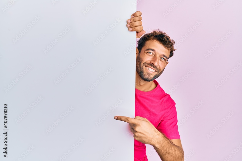 Handsome man with beard holding blank empty banner smiling happy pointing with hand and finger Handsome man with beard holding blank empty banner smiling happy pointing with hand and finger