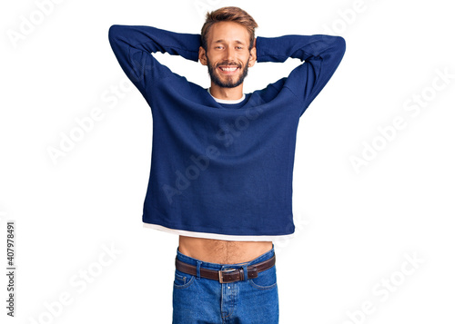 Handsome blond man with beard wearing casual sweater relaxing and stretching, arms and hands behind head and neck smiling happy