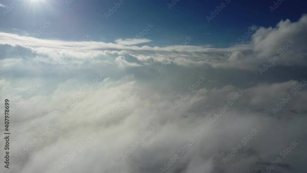 Flight in the clouds. A drone shot against a blue sky with moving clouds and sun.