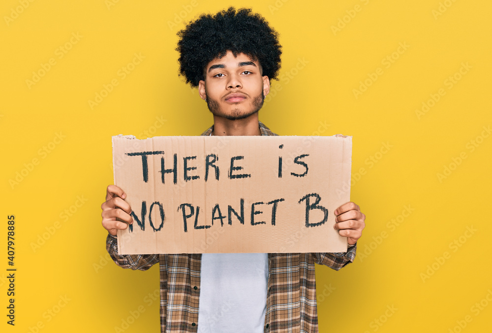 Young african american man with afro hair holding there is no planet b banner thinking attitude and sober expression looking self confident Young african american man with afro hair holding there is no planet b banner thinking attitude and sober expression looking self confident