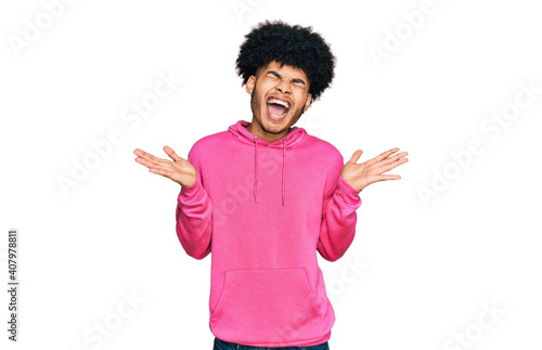 Young african american man with afro hair wearing casual pink sweatshirt celebrating mad and crazy for success with arms raised and closed eyes screaming excited. winner concept