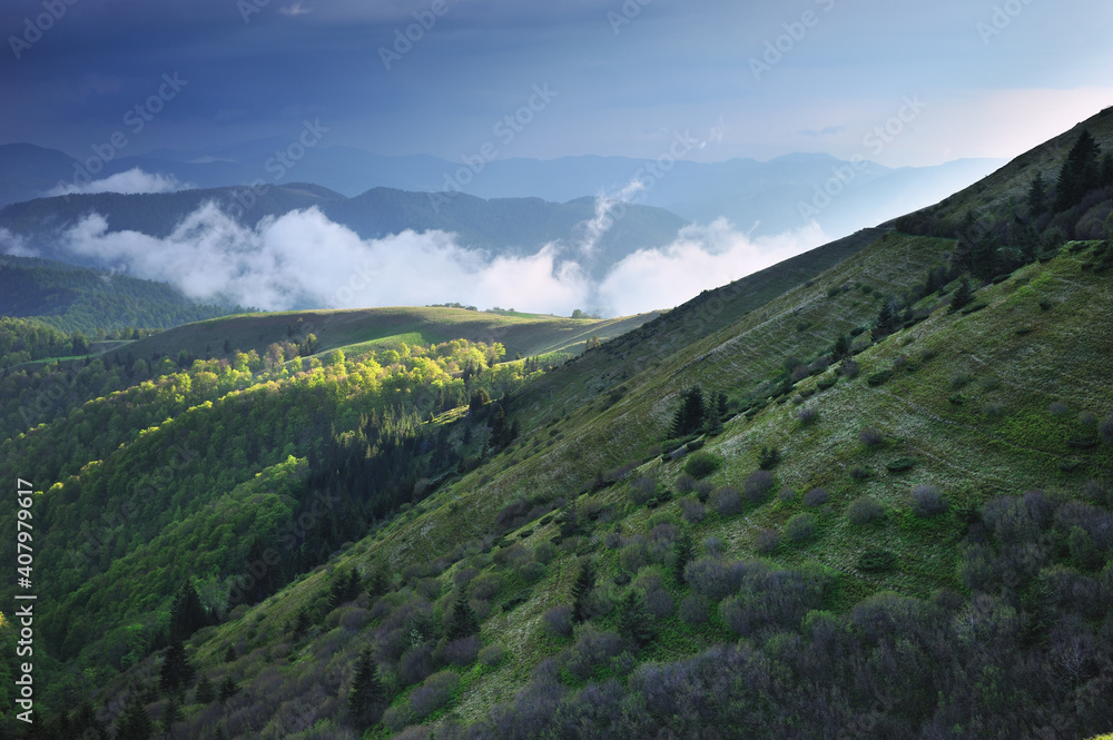 Panoramic view of a mountain range in the fog in cloudy summer weather at sunset.