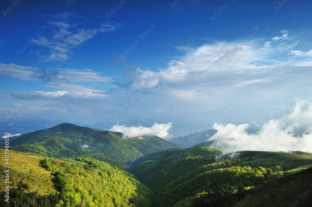 Panoramic view of a mountain range in the fog in cloudy summer weather at sunset.