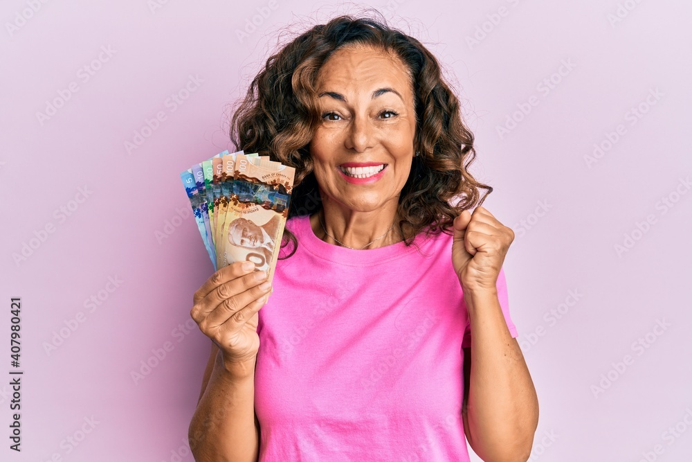 Middle age hispanic woman holding canadian dollars screaming proud, celebrating victory and success very excited with raised arm Middle age hispanic woman holding canadian dollars screaming proud, celebrating victory and success very excited with raised arm