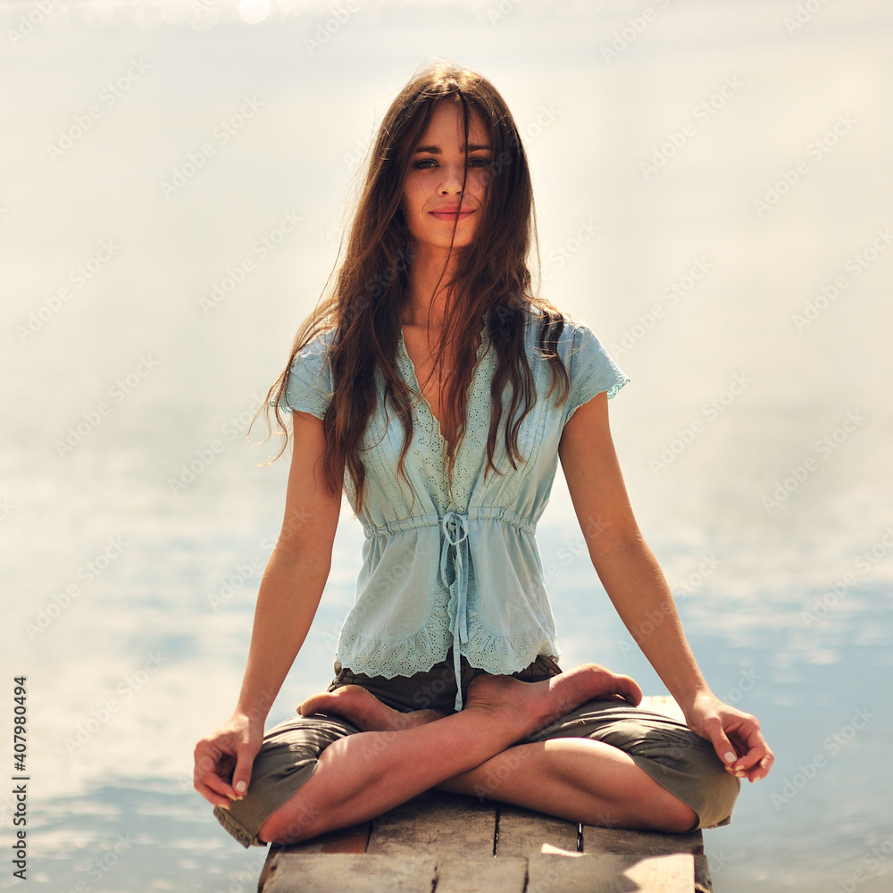Young caucasian slim woman with long brown hair doing yoga exercises on a beach at sunrise.