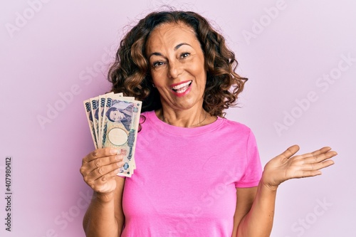 Middle age hispanic woman holding japanese yen banknotes celebrating achievement with happy smile and winner expression with raised hand