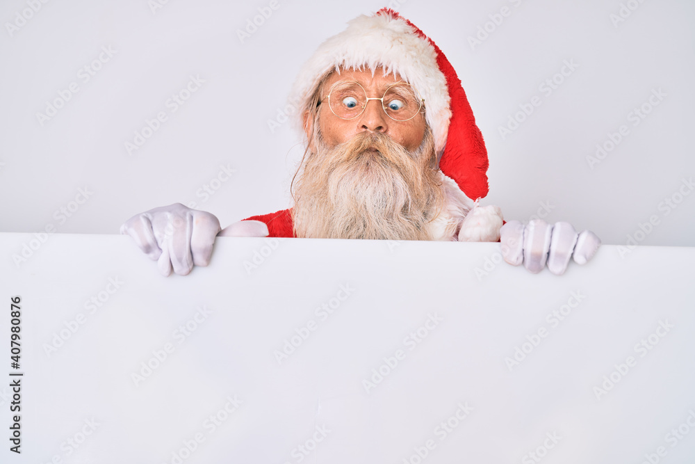 Old senior man with grey hair and long beard wearing santa claus costume holding banner making fish face with mouth and squinting eyes, crazy and comical. Old senior man with grey hair and long beard wearing santa claus costume holding banner making fish face with mouth and squinting eyes, crazy and comical.