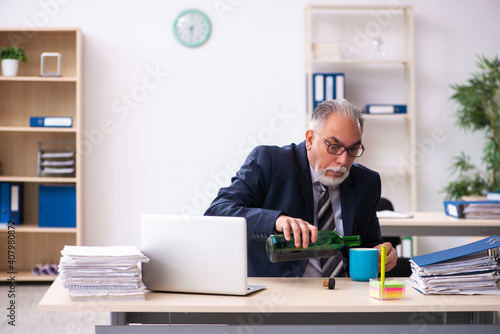 Old male employee drinking alcohol in the office