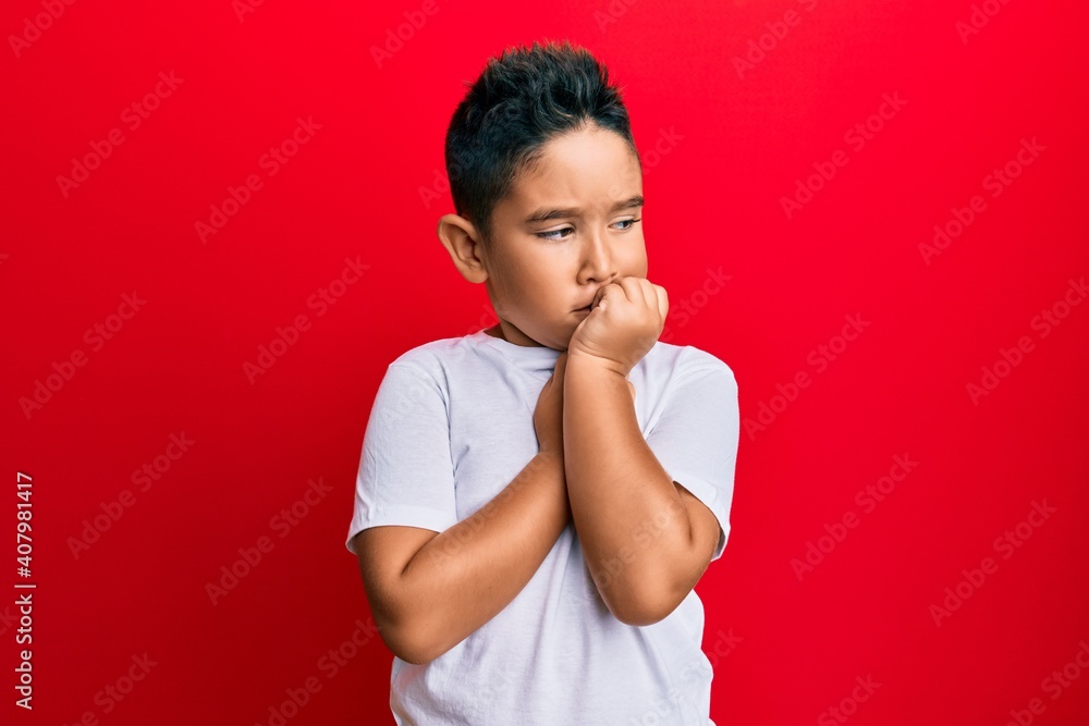 Little boy hispanic kid wearing casual white tshirt looking stressed and nervous with hands on mouth biting nails. anxiety problem. Little boy hispanic kid wearing casual white tshirt looking stressed and nervous with hands on mouth biting nails. anxiety problem.