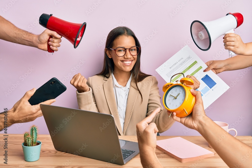 Beautiful hispanic woman working at the office under stress screaming proud, celebrating victory and success very excited with raised arms