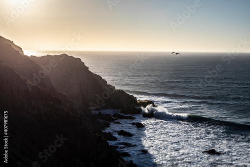 An awe sunset in an idyllic beach landscape with the sunset over the water and the sunlight generating a moody atmosphere. An amazing wil scenery with the cliffs and the sea waves splashing water photo