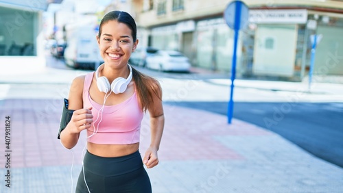 Young beautiful hispanic sport woman wearing runner outfit and headphones, smiling happy running at the town © Krakenimages.com