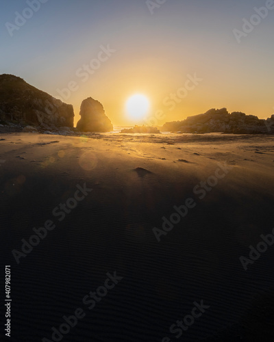 An awe sunset in an idyllic beach landscape with the sunset over the water and the sunlight generating a moody atmosphere. The long shadows of the rocks and the sand generate a texture background photo