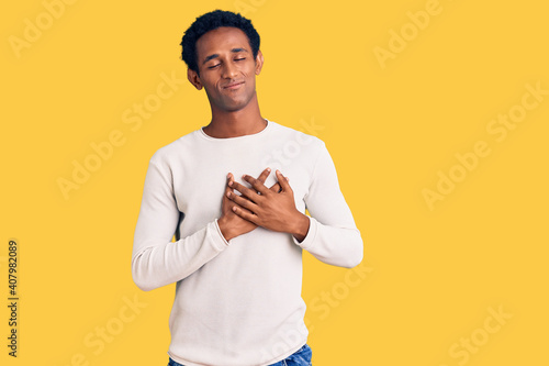 African handsome man wearing casual winter sweater smiling with hands on chest with closed eyes and grateful gesture on face. health concept.