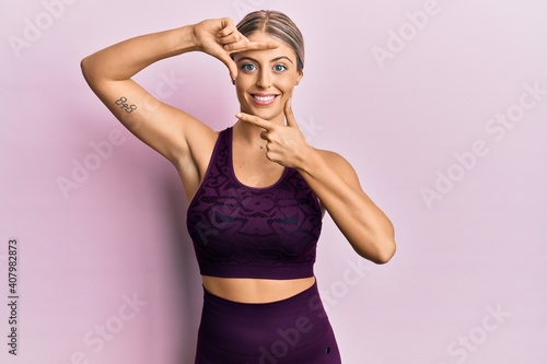 Beautiful blonde woman wearing sportswear over pink background smiling making frame with hands and fingers with happy face. creativity and photography concept.