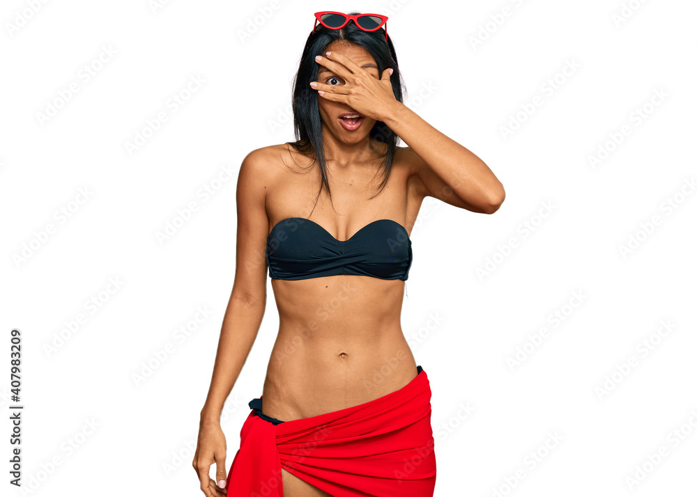Young african american woman wearing bikini peeking in shock covering face and eyes with hand, looking through fingers with embarrassed expression. Young african american woman wearing bikini peeking in shock covering face and eyes with hand, looking through fingers with embarrassed expression.