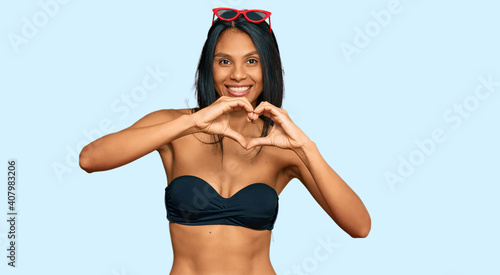 Young african american woman wearing bikini smiling in love doing heart symbol shape with hands. romantic concept. © Krakenimages.com