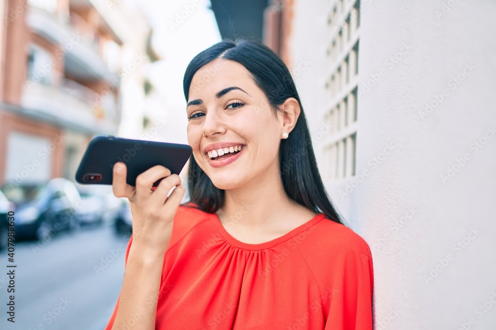 Young latin girl smiling happy sending voice message using smartphone at the city.