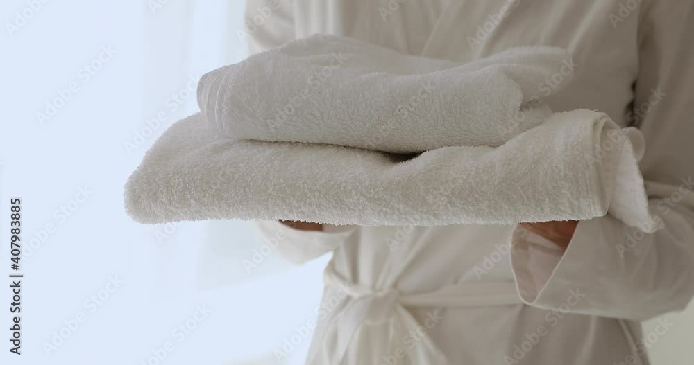 Close up young woman in white bathrobe holding soft puffy fresh towels set in hands, ready for daily hygienic activity, morning showering or evening bath, spa procedure, laundry service concept. Close up young woman in white bathrobe holding soft puffy fresh towels set in hands, ready for daily hygienic activity, morning showering or evening bath, spa procedure, laundry service concept.