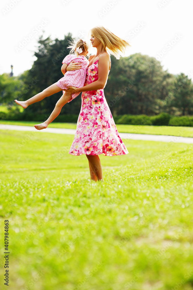 Young blonde mother in dress playing with little kid blonde daughter in the park. Young blonde mother in dress playing with little kid blonde daughter in the park.