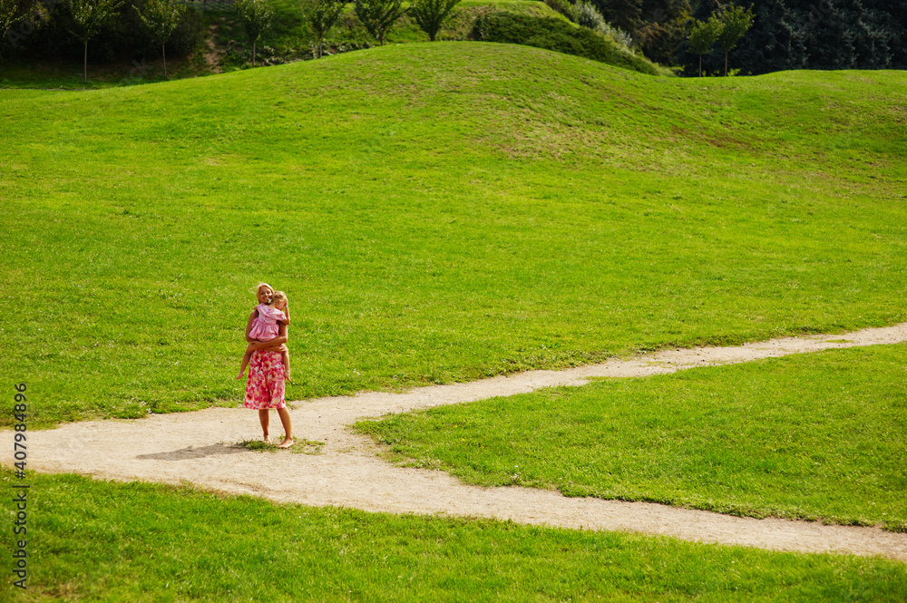 Young blonde mother in dress playing with little kid blonde daughter in the park. Young blonde mother in dress playing with little kid blonde daughter in the park.