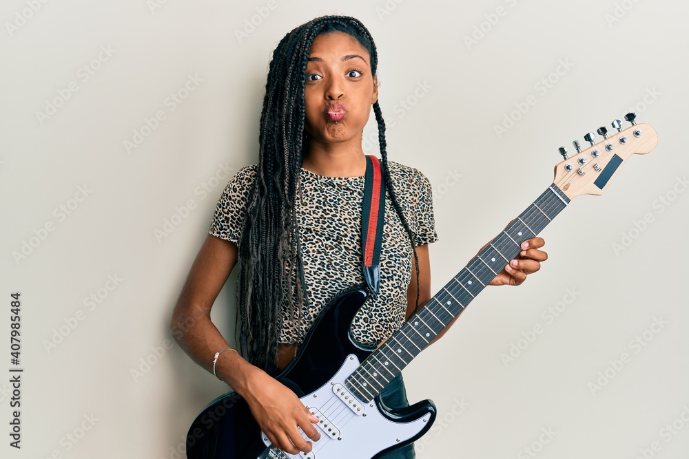 African american woman playing electric guitar puffing cheeks with funny  face. mouth inflated with air, catching air. Stock-Foto | Adobe Stock