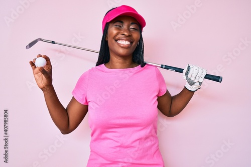 African american golfer woman with braids holding golf ball winking looking at the camera with sexy expression, cheerful and happy face.