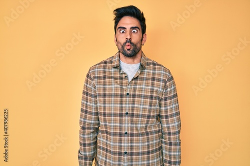 Handsome hispanic man with beard wearing casual clothes making fish face with lips, crazy and comical gesture. funny expression.