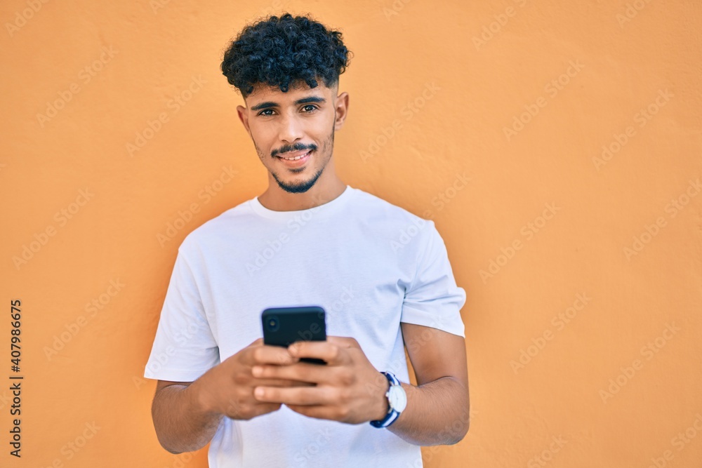 Young arab man smiling happy using smartphone leaning on the wall. Young arab man smiling happy using smartphone leaning on the wall.