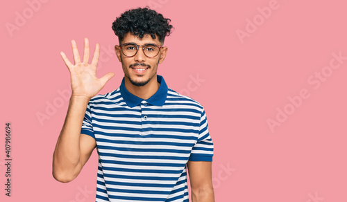 Young arab man wearing casual clothes and glasses showing and pointing up with fingers number five while smiling confident and happy.