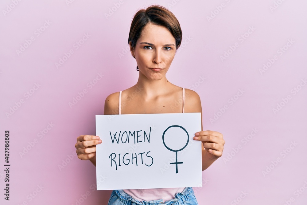 Young brunette woman with short hair holding woman rights banner skeptic and nervous, frowning upset because of problem. negative person. Young brunette woman with short hair holding woman rights banner skeptic and nervous, frowning upset because of problem. negative person.