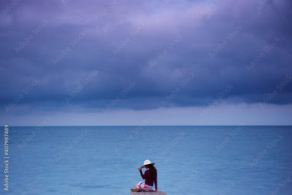 Young caucasian woman in a hat sitting on a pier near the sea.