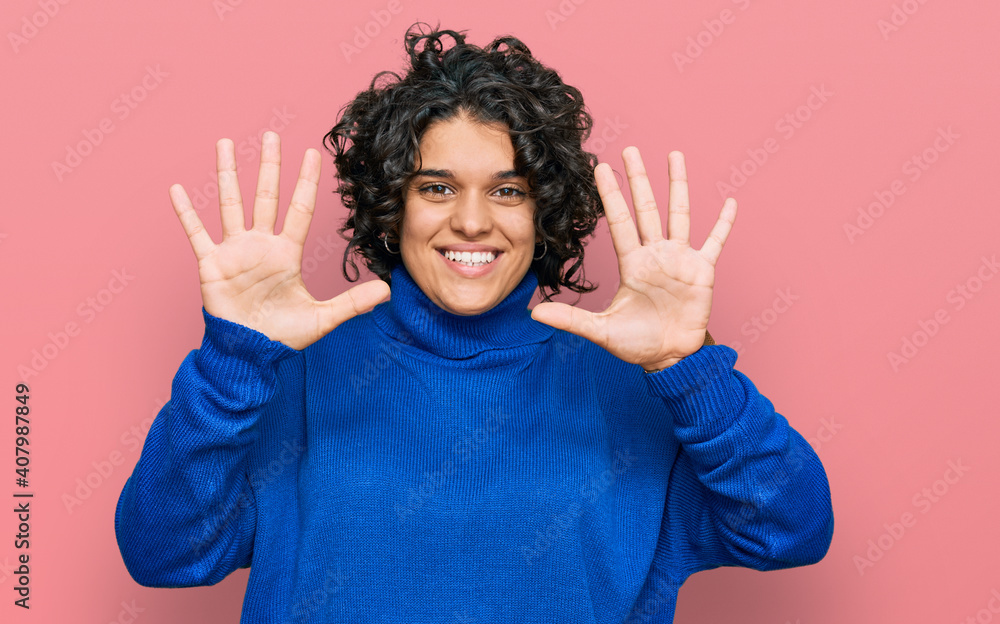 Young hispanic woman with curly hair wearing turtleneck sweater showing and pointing up with fingers number ten while smiling confident and happy. Young hispanic woman with curly hair wearing turtleneck sweater showing and pointing up with fingers number ten while smiling confident and happy.