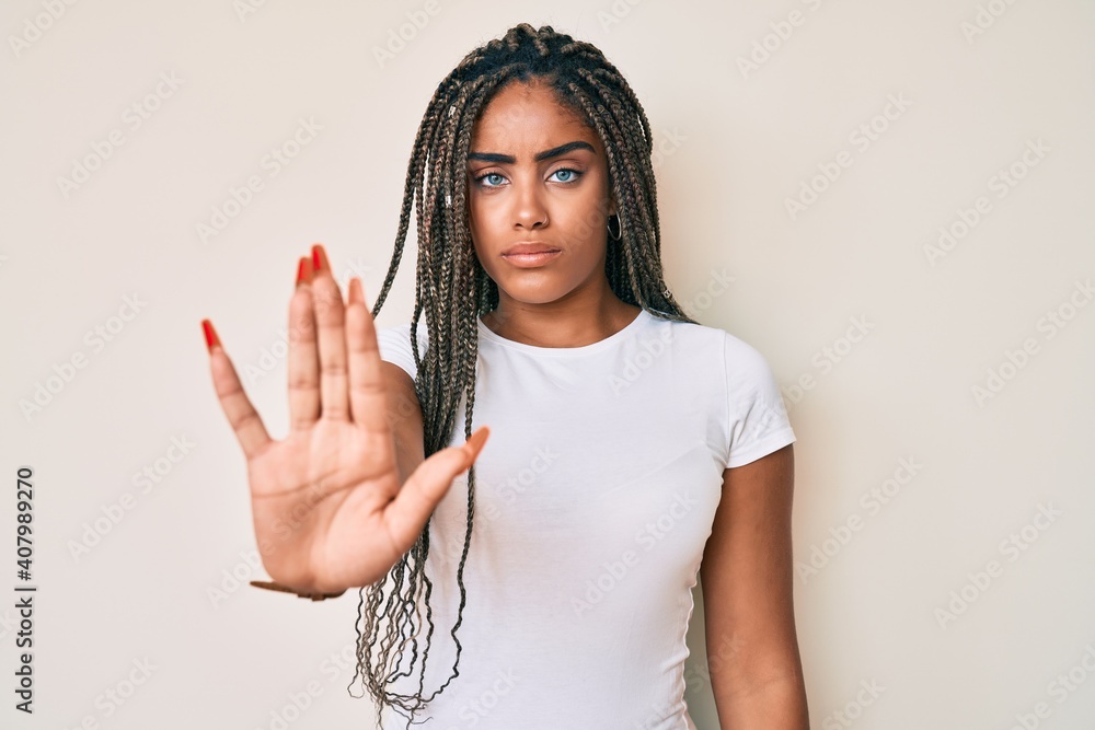Fototapeta premium Young african american woman with braids wearing casual white tshirt doing stop sing with palm of the hand. warning expression with negative and serious gesture on the face.