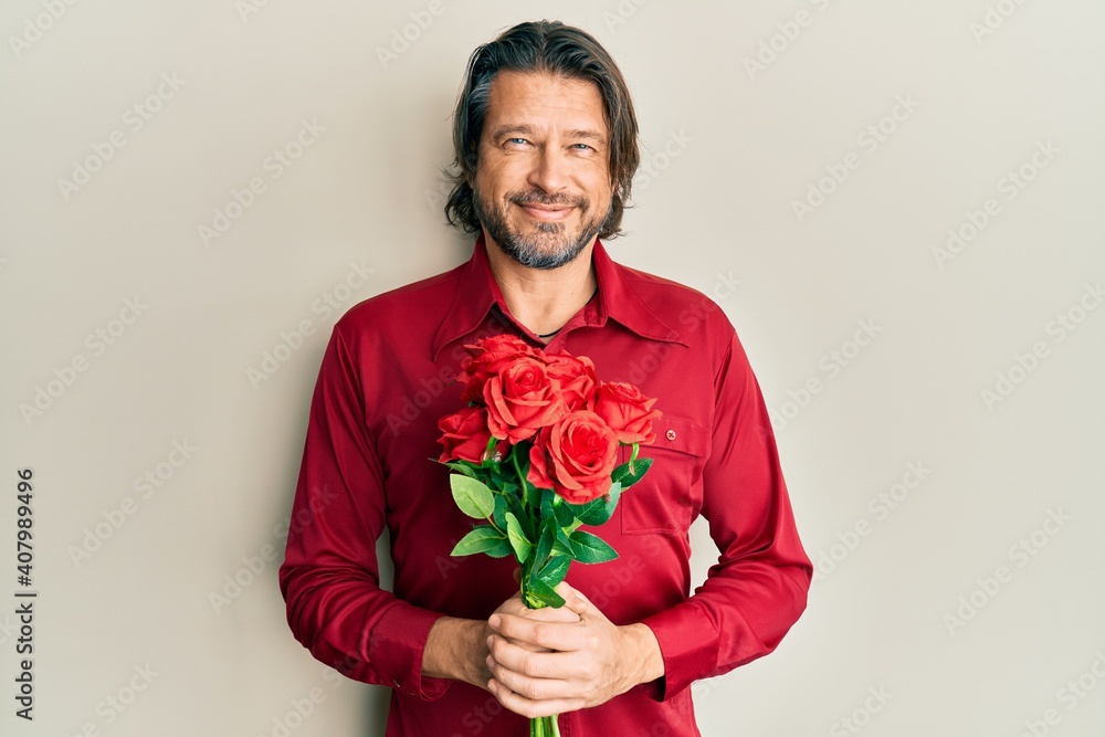Middle age handsome man holding bouquet of red roses smiling with a happy and cool smile on face. showing teeth. Middle age handsome man holding bouquet of red roses smiling with a happy and cool smile on face. showing teeth.