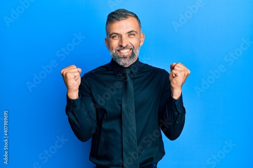 Middle age handsome man wearing business shirt and tie celebrating surprised and amazed for success with arms raised and open eyes. winner concept.