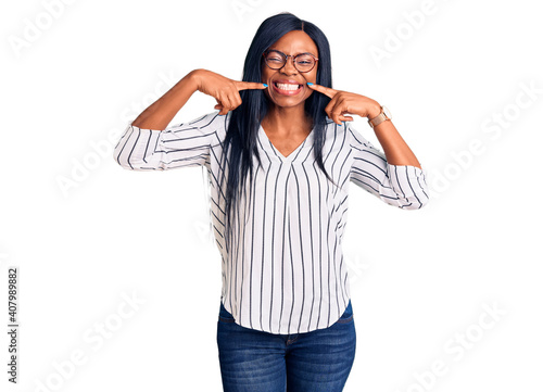 Young african american woman wearing casual clothes and glasses smiling cheerful showing and pointing with fingers teeth and mouth. dental health concept.