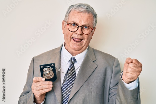 Senior grey-haired man holding detective badge screaming proud, celebrating victory and success very excited with raised arms © Krakenimages.com