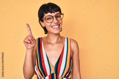 Beautiful brunettte woman wearing casual clothes and glasses pointing finger up with successful idea. exited and happy. number one.