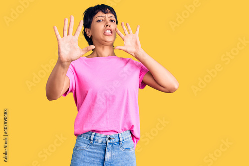 Young brunette woman with short hair wearing casual clothes afraid and terrified with fear expression stop gesture with hands, shouting in shock. panic concept.