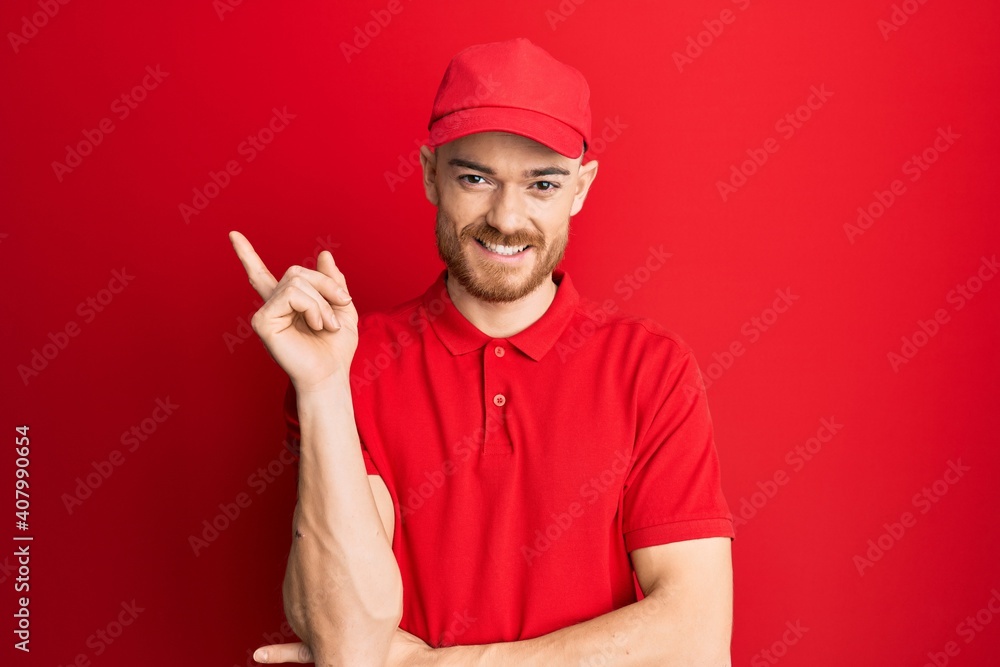 Young redhead man wearing delivery uniform and cap smiling happy pointing with hand and finger to the side Young redhead man wearing delivery uniform and cap smiling happy pointing with hand and finger to the side