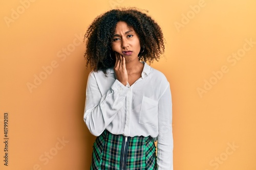 Beautiful african american woman with afro hair wearing scholar skirt touching mouth with hand with painful expression because of toothache or dental illness on teeth. dentist © Krakenimages.com